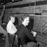 Två växeltelefonister i arbete. Trots branden, i Televerkets lokal på Nygatan, så fortsätter arbetet vid växelborden.
Läs om Telefonen i Arboga och branden på Televerket 1956 i Arboga Minnes årsbok 1993.