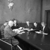 Valnämnden sammanträder i drätselkammarsalen på Rådhuset.
Från vänster: Vidar Adolfsson, Georg Linell, borgmästare Daniel Ekelund (ordförande), Emanuel Carlsson, Erik Ring och Mary Zilo (kommunaltjänsteman)
På väggen hänger en pendyl.