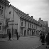 Öhrman & Melanders butik på Nygatan firar 50-årsjubileum. I skyltfönstret ses en skyltdocka. Affären säljer kläder. 
Folkliv på gatan; människor promenerar och cyklar. Järnaffären ses en bit bort.