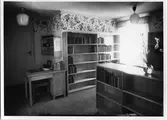 Biblioteket, interiör. Bokhyllor med böcker, ett skrivbord. Påskris i en vas.
Troligen från biblioteket på Nygatan.
Baksidan av detta fotografi kan ses på AKF-14450