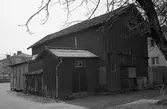 Exteriör. Uthus/förråd. Två soptunnor står utanför. Intill uthuset ses två nyare flerfamiljshus.
Fotografens anteckning: Dokumentation av fastigheter i kvarteren söder och norr om ån. Bilder och beskrivningar finns på Arboga museum.