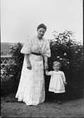 Christiane Liljefors med sin dotter Marit står i trädgård, sannolikt hos Christianes föräldrar i Stavanger, Norge