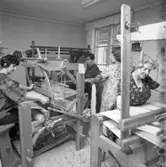 Husmodersföreningens vävstuga. Två kvinnor väver och två kvinnor hjälps åt att dra på en väv.