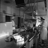 Interiör från köket på det nya ålderdomshemmet, Strömsborg. Tre kvinnor i arbete.
Till vänster står Olga Larsson och bakar sockerkakor. Anna-Lisa Söderberg skymtar bakom hushållsmaskinen. Margit Wirzelius rör om i grytan.