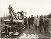 Grimman lossas från betongslipern av Henning Eriksson och traktorförare Bo Johansson är redo att placera ut nästa sliper. Bengt Peel, Ingvar Svensson, Georg Storm, Gösta Johansson, Evert Gustavsson och Lars Olsson övervakar.