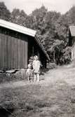 Porträtt av två små flickor på gården Christinedal i östra Mölndal på 1950-talet. I bakgrunden ses en av gårdens ekonomibyggnader. Gården har gett namn åt området Kristinedal och var belägen i vinkeln mellan nuvarande Rådavägen och Brovaktaregatan. År 1960 såldes gården till Fastighetsbolaget Betongblandaren (Skånska Cementgjuteriet) och revs när det nuvarande bostadsområdet anlades.