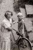 En kvinna och en pojke med cykel fotograferade på gården Christinedal i östra Mölndal på 1950-talet. Gården har gett namn åt området Kristinedal och var belägen i vinkeln mellan nuvarande Rådavägen och Brovaktaregatan. År 1960 såldes gården till Fastighetsbolaget Betongblandaren (Skånska Cementgjuteriet) och revs när det nuvarande bostadsområdet anlades.