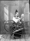 Ateljéporträtt - Lotten Lindgren klädd i folkdräkt spinner, Dalarna 1893
