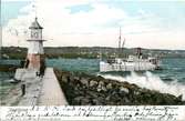 Ett vykort skickat 1906-02-07 med motiv från Hamnpiren och fyren i Jönköpings hamn. En ångare är på väg in och vågorna på Vättern slår mot strandskoningen.