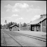 Vy över Dala Finnhyttan stationshus och godsmagasin med Garpenberg kyrka i bakgrunden.