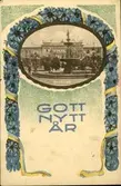 Vykort med motiv av en blomsterbåge som har en infälld bild av Vängåvan och med texten: Gott Nytt År.