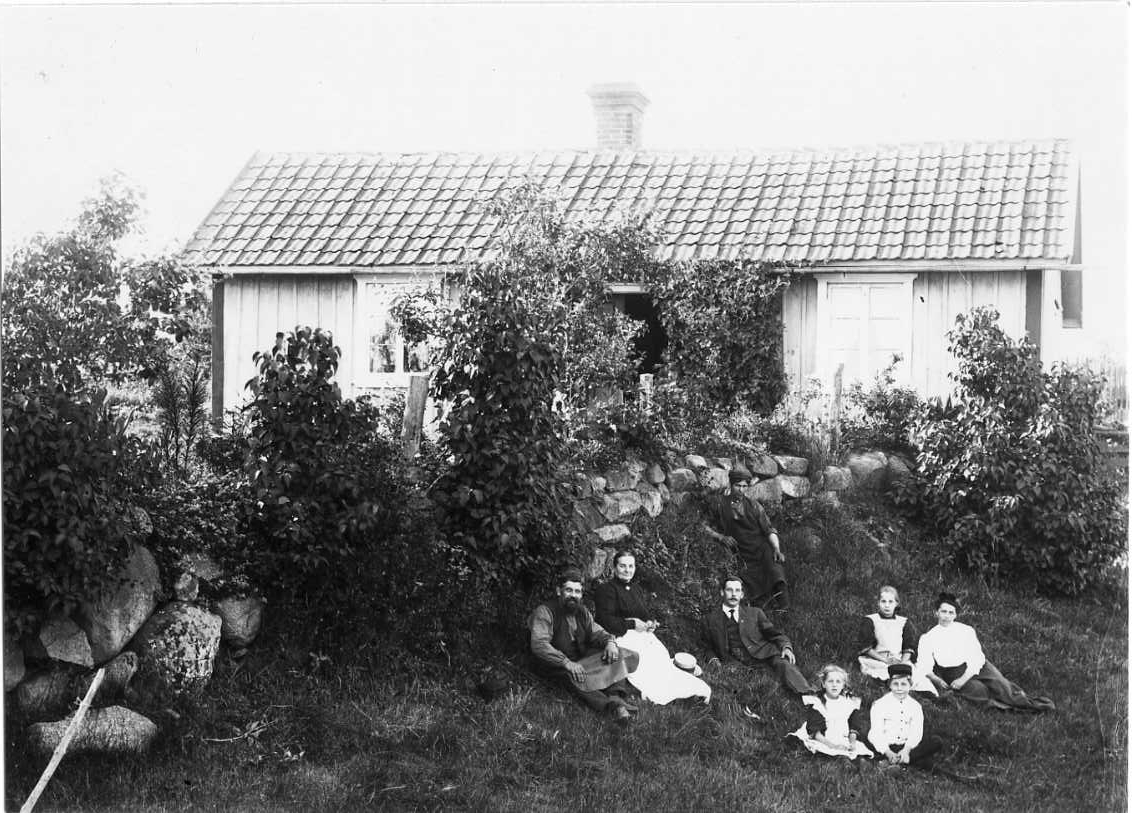 Calla Helena Sundbeck, The Roman family sits in a dragonfly below a stone wall. Behind it is the family house. From the left the blacksmith Viktor Roman with foreskin, the wife Augusta Roman with light apron electricity possibly canvas over his legs, son Erik in fine clothing. At the very front are the children Karin and…