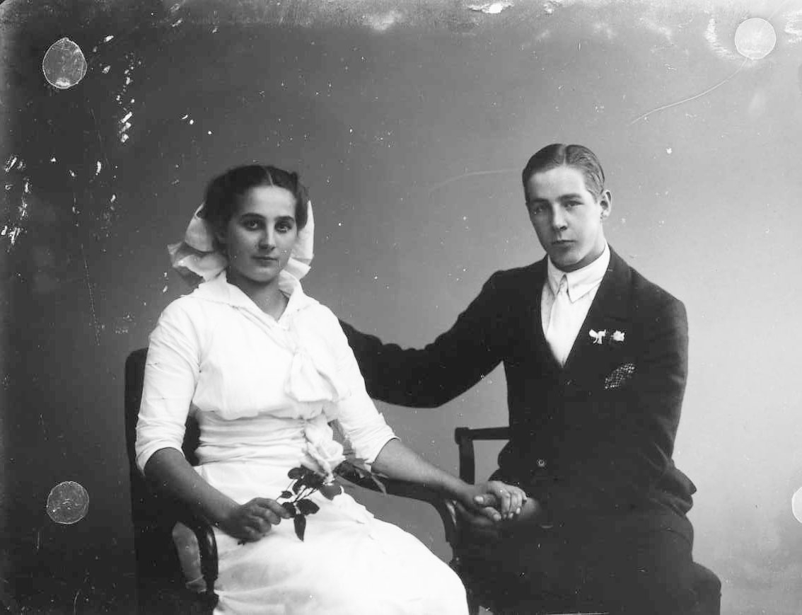 Calla Helena Sundbeck, Group image with the siblings Karin and Gösta Roman. They sit next to each other and hold each other’s hand. Karin is wearing a bright dress and possibly a big bow in his neck. She holds a white rose in her right hand. Gösta has a suit with a bright dotted shirt, a light tie, a dotted handkerchief …