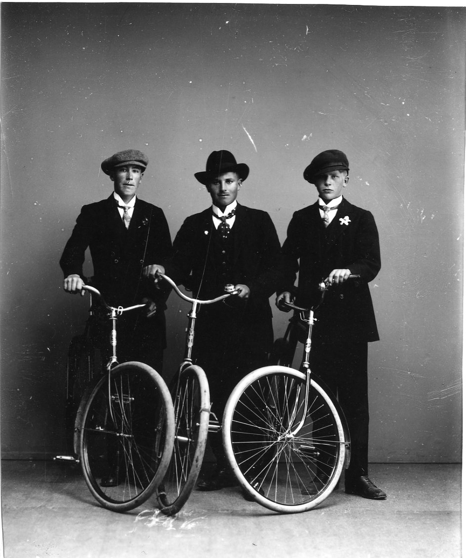 Calla Helena Sundbeck, Tre välklädda unga män, med slips och hatt respektive keps, står med varsin cykel i ateljén. De är från vänster Erik Lago från Joenstorp, Einar Johansson från Fallet och Axel Johansson från Fallet.