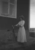 Dam med cykel vid husvägg.
