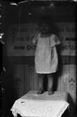 Ett barn står på ett bord med en broderad bonad bakom sig, Östhammar, Uppland