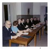 En grupp (S)-politiker sitter vid uppställda bord i Kållereds kommunalhus på Streteredsvägen 3 (Vommedal Västergård) år 1969. Från vänster: Harry Johansson (1902 - 1977), Hildur Berntsson (1925 - 1997), Ragnar Andersson (1917 - 1997), Sigvard Larsson (1919 - 1991), Evert Eliasson (1912 - 1993), Ivar Andersson (1913 - 2004), Per-Olof Lundberg (1930 - ) samt Erik Svärd (1921 - 1983). Stående är Signe Fredriksson (C) (1901 - 1992).