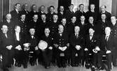 Gruppbild av män tillhörande brandstyrelse och brandkår. Tre av männen på främsta raden håller i silverföremål.