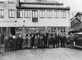 Personalgruppbild från Alingsås Bil- och motorverkstad, ca 1946-47. 30 män och 2 kvinnor står på två led framför verkstadbyggnaden. Högst på byggnaden en skylt med texten 