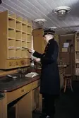 Seriebild ;M 25. I en ålderdomlig järnvägspostkupé, i
Järnvägsmuseum i Tomte-boda i Solna, arbetar en postiljon med
brevsortering. I den arrangerade situa-tionen agerar fotobiträdet
Gunnar Svensson, Postens Fotografer, i en uniform från Postmuseum.