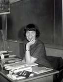 Lärare Inger Claesson Leidenborg (1932 - 1984) sittandes vid en kateder i Kålleredskolan/Brattåsskolan cirka 1965. Bakom henne ses 