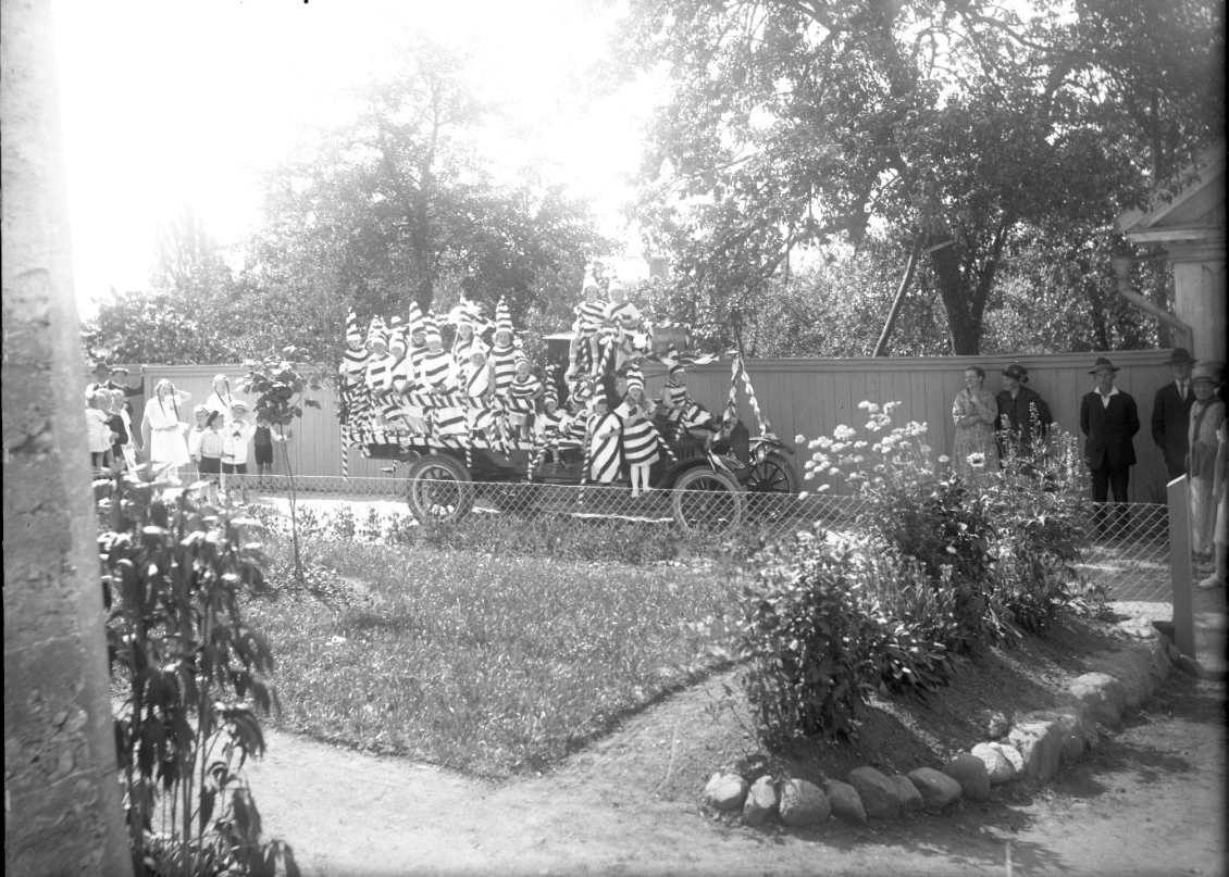 Calla Helena Sundbeck, A truck with a flak loaded with children in polish striped clothes. On the bonnet is Olof Fong. The picture is probably on Bergsden. On the right stands a group of adults, men and women and watching. On the left, behind the car, children stand watching.