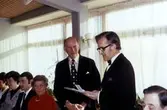 Avtackning av skolvaktmästare Alvar Andersson i matsalen på Brattåsskolan, cirka 1970. Från vänster: okänd, lärare Ann-Marie Fälthammar, rektor Rolf Sandström, Elsa Andersson (Alvars hustru), stående: Alvar Andersson (1909-1999) och rektor Gunnar Hillerström samt Holger Bornell från Skolstyrelsen.