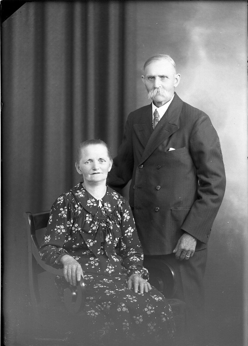 Calla Helena Sundbeck, Ett äldre par. Mannen med mustasch står vid en sittande kvinnas vänstra sida. De är bägge finklädda. Hon bär en klänning med blommönster. Mannen är möjligen Emil Frid från Prästekvarn i Brötjemark i Ölmstad socken eller är hans namn Forsander.