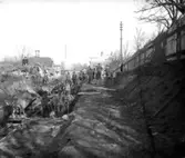 Här pågår anläggningsarbetet med den nya bansträckningen söderut från Varbergs station. Bilden är tagen väster om kvarteret Prästgården och i bakgrunden syns missionshuset i kv Skepparen.  Järnvägsarbetarna använder handredskap och jordmassorna fraktas i vagnar som går på räls. Den nya sträckningen invigdes 1920.