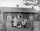 Exteriör av det spånklädda boningshuset på Bjuråsen, som var fotografen Erik Ruds hem.
Framför huset familjerna Torell och Ek.