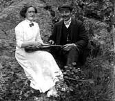 ETT PAR SITTER VID ETT BERG, HON SPELAR FIOL.