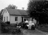 Familj sittandes i trädgården framför bostadshuset.
Morföräldrar till Gösta Ivarsson.
Juli 1913.
