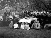 MÅNGA MÄNNISKOR I OLIKA ÅLDRAR SAMLADE VID ETT DUKAT BORD I TRÄDGÅRDEN, SANNOLIKT EN SLÄKTGRUPP.

Fotot taget i aug. 1917.