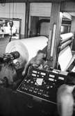 Män i arbete vid rullmaskin 5 på pappersbruket Papyrus i Mölndal, hösten 1970. Maskinen rullar ner en tambour till smårullar.
