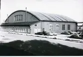 Västerås Hässlö 5:1 Hangar K0077.081 vid F1 Västerås Flygflottilj
1960-talet?
Bilar står parkerade utanför hangaren.