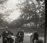 Två män i trädgård lyssnande på fonograf, Lillhärad, ca 1910.