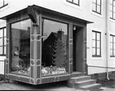 Den spektakulära entrén till Kooperativa AB i Varberg, hörnet Götagatan-Engelbrektsgatan, kv Kaninen 3. Hörnet kragar utanpå fasaden runt hörnet med två stora skyltfönster som inramas av listverk med omväxlande cirklar och rektanglar. På en cirkel sitter en reklamskylt för 