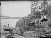 Josef Edhlund sitter på klipporna tillsammans med en man och två kvinnor. Två barn är vid en båt , Östhammar, Uppland