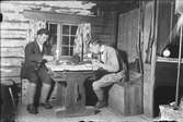 Josef Edhlund sitter och dricker kaffe tillsammans med en man i en timmerstuga, Östhammar, Uppland