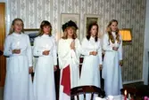 Luciatåg i Brattåshemmets matsal, december 1978. Linda Dahlgren är Lucia, övriga namnuppgifter saknas. Troligtvis har kvinnorna fått var sitt halssmycke som gåva, vilket de bär runt halsen. Relaterade motiv: A1854 samt A1860.