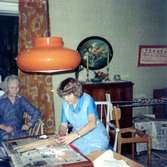 Ljusstöpning i Brattåshemmets dagrum år 1979. Från vänster ses Agnes Ekstedt (1898 - 1984) och terapibiträde Maj Britt Rickard. I bakgrunden ses byrå, oval blomstertavla och ljusstakar som har tillhört Selma Börjesson från Högkullen, Tulebo. Relaterat motiv: A1875.