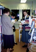 Tre kvinnor står och läser bland hyllorna, Kållereds bibliotek 1990-tal. Ett arrangemang anordnat av Hembygdsföreningen. Till höger ses Karin Gustafsson från Hembygdsföreningen.
