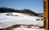 Vy från balkong på Vommedalsvägen, där människor åker pulka och skidor vid Himlabacken (ner från Kållereds kyrka) i Vommedal, cirka 1975. Där ligger idag Vommedals näridrottsplats.