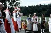 Dräktparad med folkdräktsklädda män och kvinnor en hembygdsdag på Långåker år 1984. Från vänster: 1. Okänd, 2. Okänd, 3. Rigmor Lindqvist, 4. Lily Edvardsson med Hallands-skylt, 5. Flicka, 6. Kvinna med Lapplands-skylt, 7. Sandberg med Ångermanlands-skylt, 8. Hällesåkers spelmanslag.