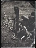 En pojke har somnat vid en sten bredvid ett staket.