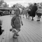 Danslek med barn och vuxna. Skansen. Liten flicka ser på.