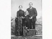 Familjebild. Familjen Thorsson. Föräldrar med en gosse mot skogsfond och rekvisita som förstärker intrycket av att de är utomhus.