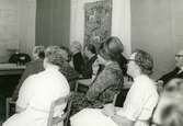 Diabildsvisning av prästfrun Märta Lindman (ej i bild) i matsalen på Brattåshemmets ålderdomshem, 1960-tal. Från vänster med vända ryggar: Okänd kvinna i vit rock, praktikant Lena Englund samt vårdbiträde Valborg Smitt (1901 - 1986) i vit rock.