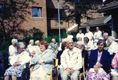 Boende på Brattåsgårdens äldreboende sitter utomhus då det firas midsommar, 1990-tal. Främre raden från vänster: 1. Hulda Olsson, 2. Gunvor Olsson, 3. Okänd, 4. Gunvor Johansson. Andra raden: 1. Aina Olsson (1917 - 2007), 2. Karin Zackrisson, 3-5. Okända, 6. Anna Maj Johansson, 7. köksbiträde Edit Johnsson, 8. Eva, 9. Oskar och Svea Jonasson.