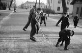 Några barn spelar bandy på Oxtorgsgatan i Jönköping. I bakgrunden ligger Västra torget och långt bort syns tornet på Brandstation .